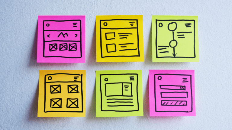 A set of sticky notes on a wall, with application wireframes drawn on them in marker