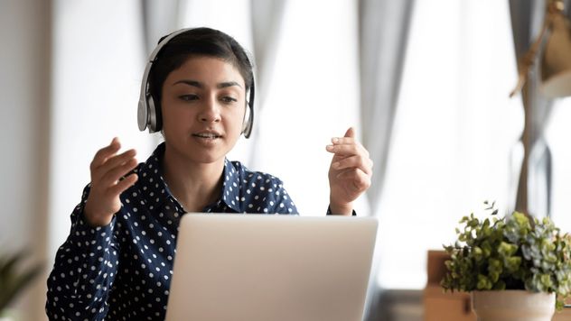 A woman sitting at a desk, using her laptop and talking with a headset