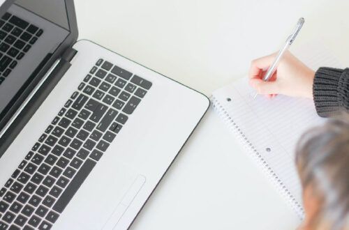 woman writing on notepad with laptop nearby