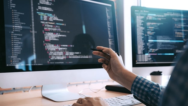 A programmer pointing to computer code on a desktop screen