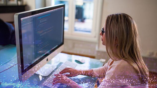 A woman sitting at a desk, typing in computer code