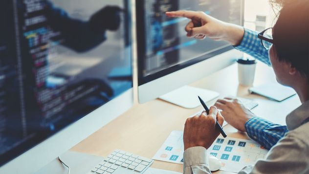 Developers sitting at a desk pointing to computer code