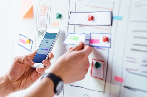 A person holding a mobile phone against paper prototypes pinned on a board