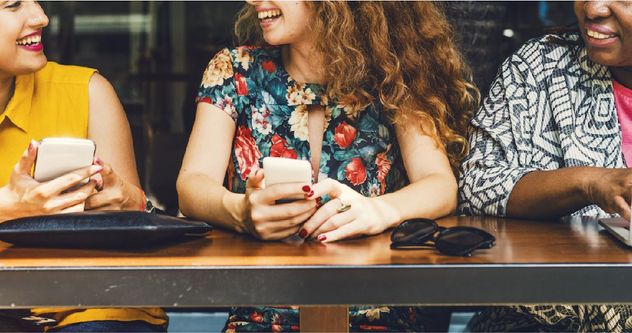 Three smiling people sitting at a table using mobile devices